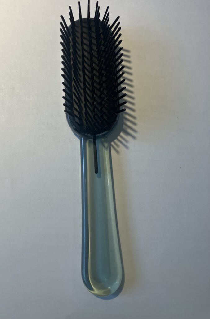 A close-up of a black hairbrush with fine bristles against a plain background.