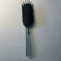 A black hairbrush with a transparent handle on a white surface.